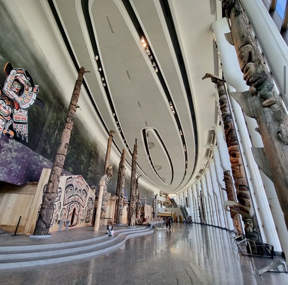 Totem poles, Indigenous art, and decorative ceiling inside a large hall of the Canadian Museum of History.
