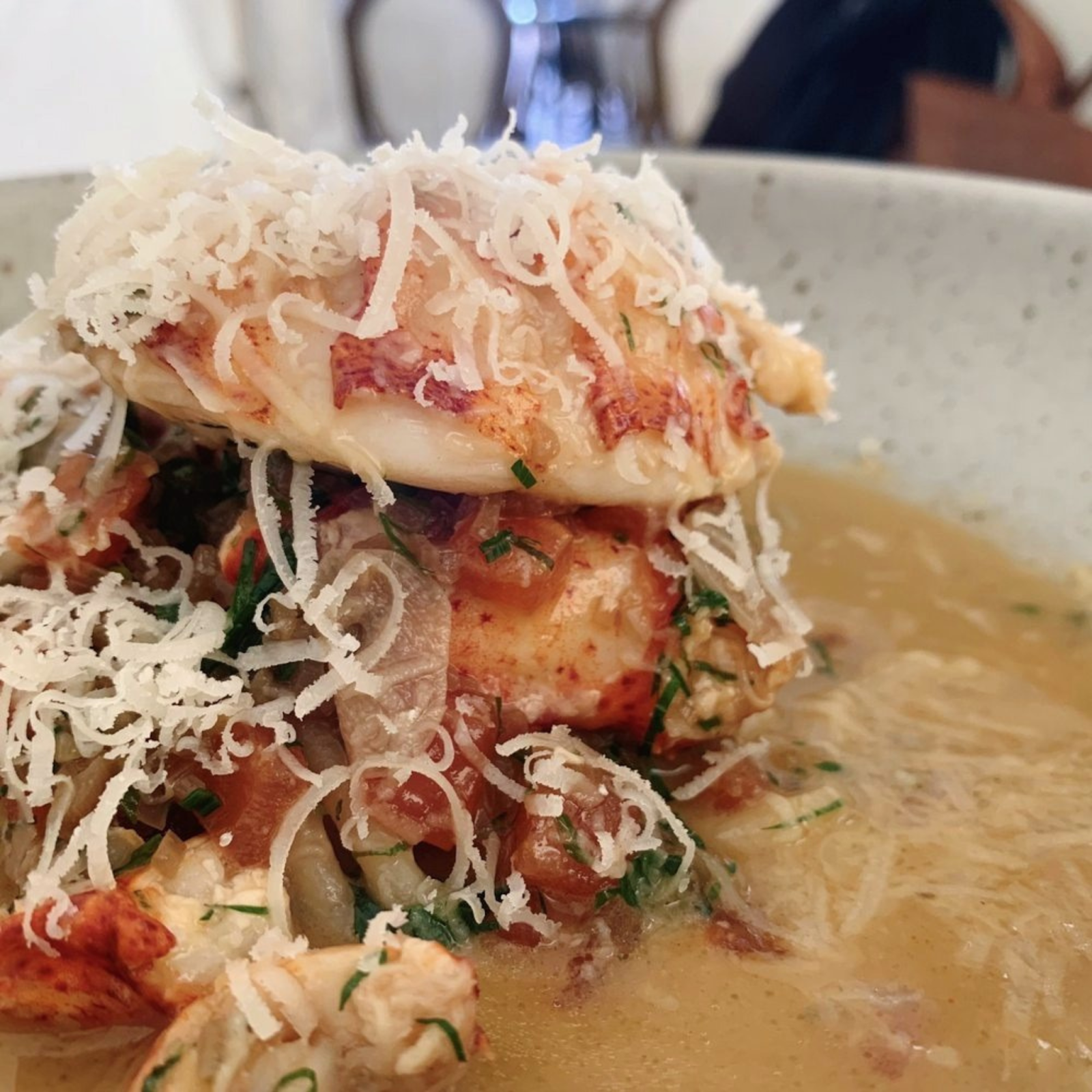 Lobster and shaved parmesan piled high on top of pasta in a bowl with sauce.